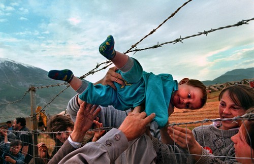 Agim Shala, 2 years old, is passed thru the barbed wire fence.